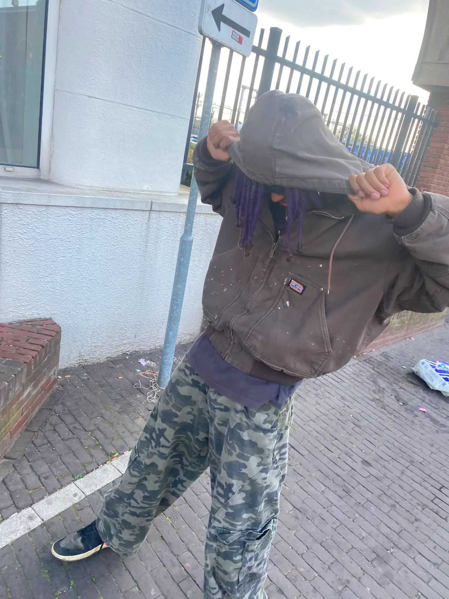 Artist pulling hood over face on a brick street